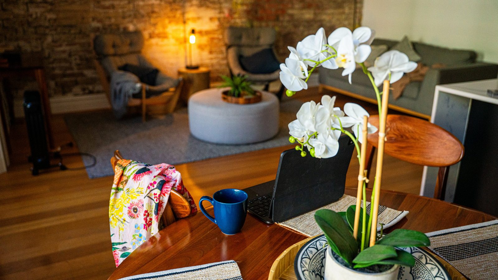 A home dining table with an orchid, a mug and a bright floral scarf on the chair