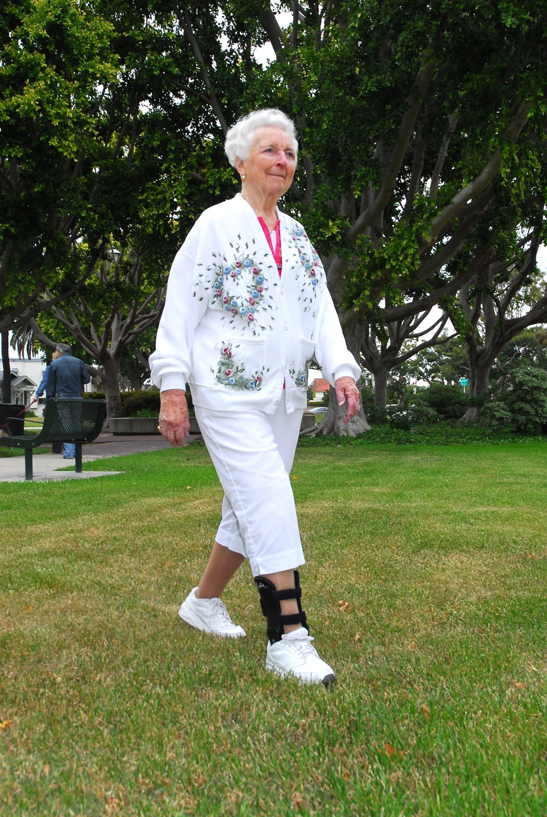 An older woman walking in a park wearing a Richie Brace