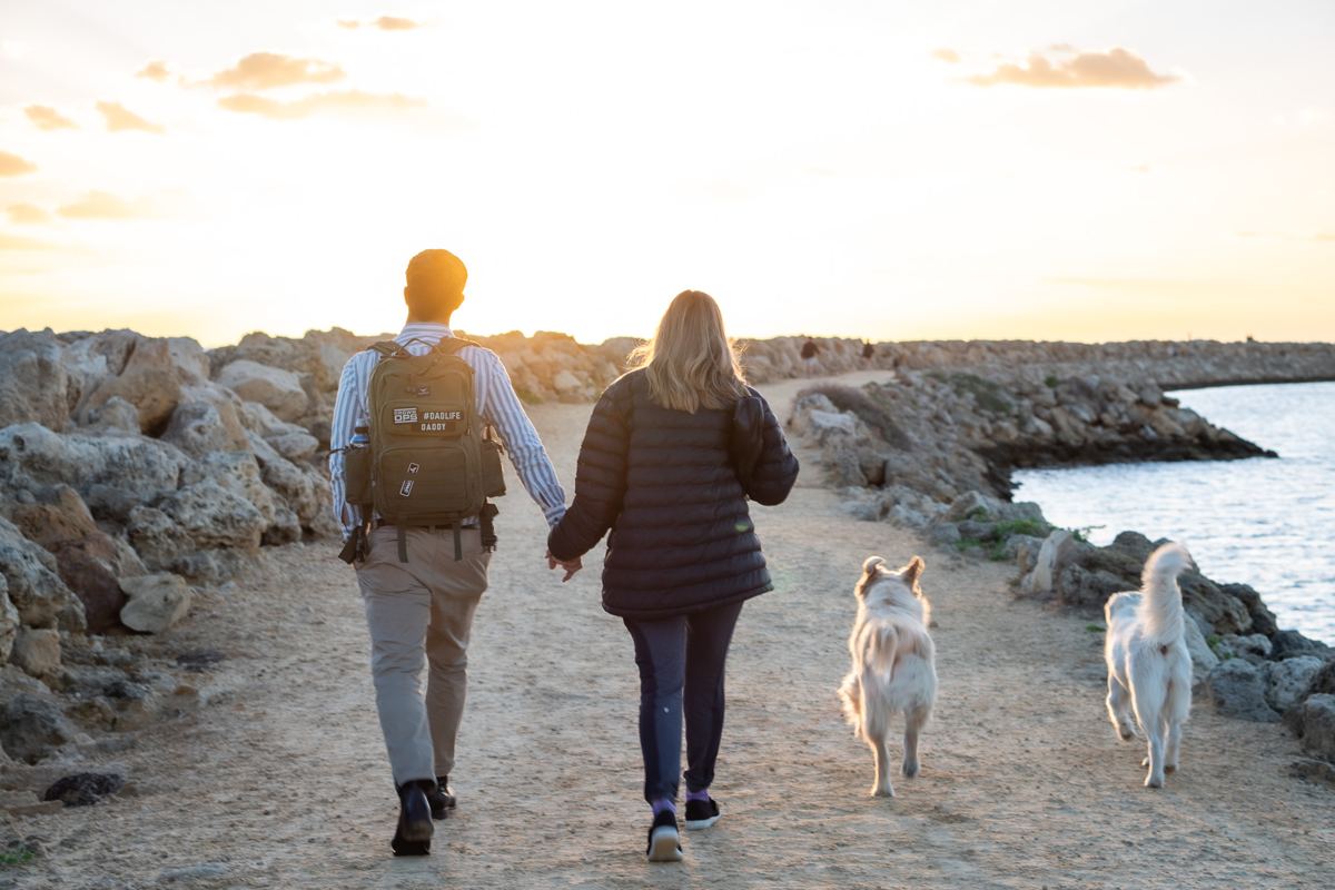 Couple walking two dogs along a coastal path at sunset